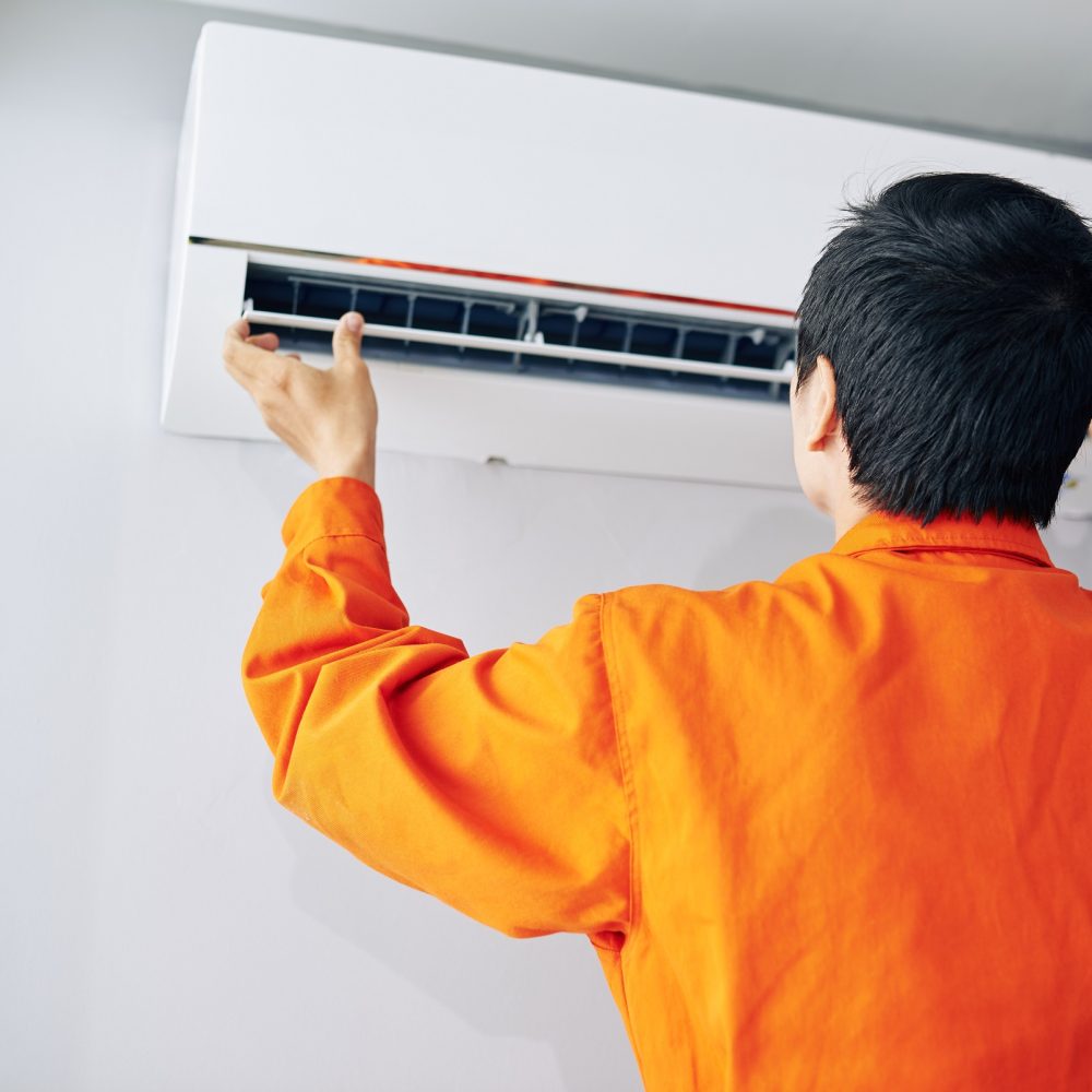 Repairman in orange uniform installing or checking air conditioner in apartment of client