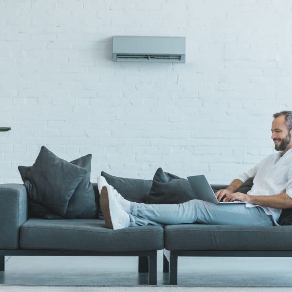 handsome-man-working-with-laptop-on-sofa-with-air-conditioner-on-wall-at-home-1-1024x684